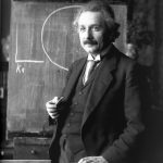 Albert Einstein standing in front of chalkboard